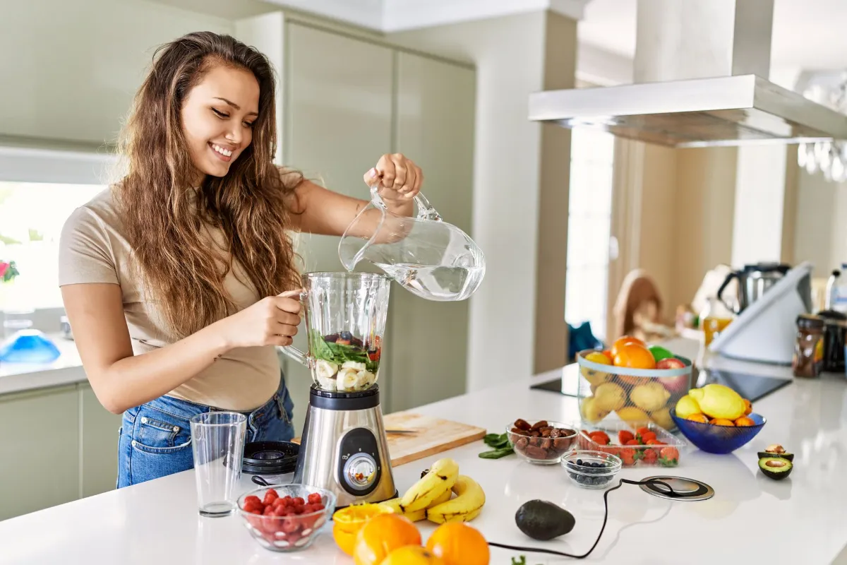 Water Filters Australia-Filtered Water makes smoothies better Young beautiful hispanic woman preparing vegetable smoothie pouring water on blender at the kitchen