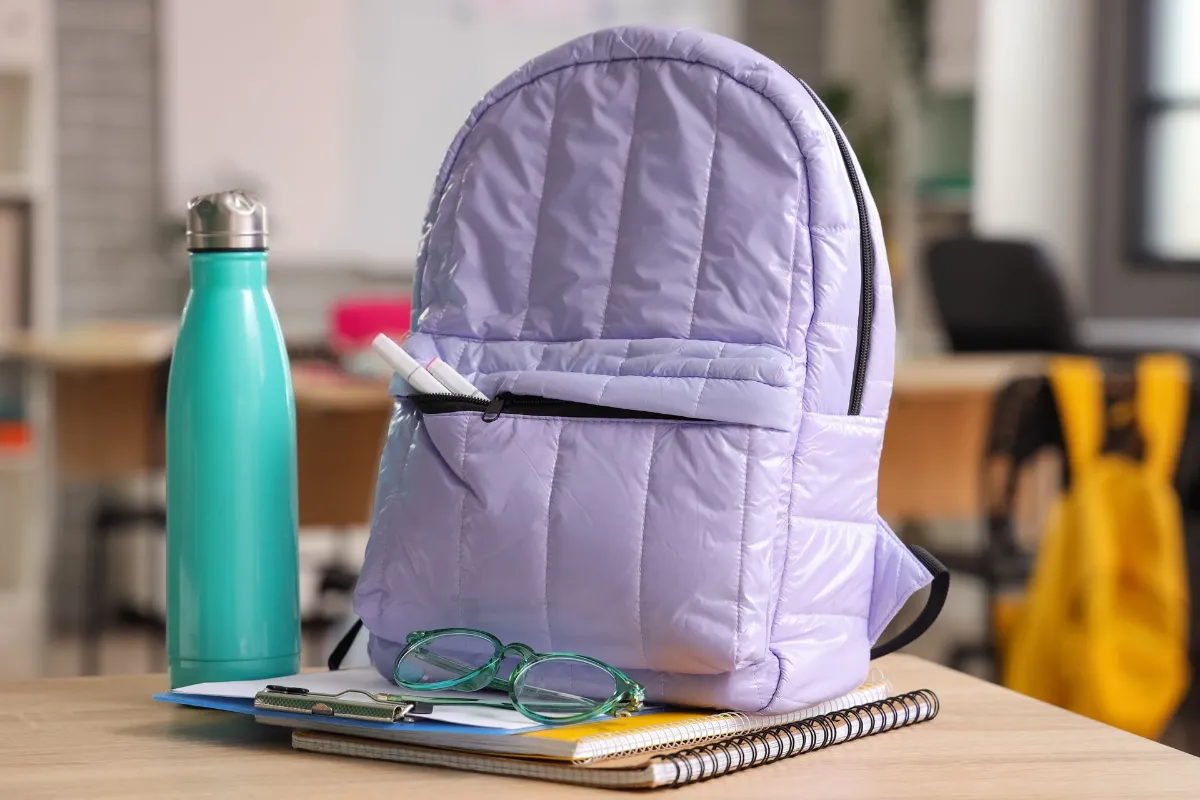 Lilac backpack with eyeglasses and water bottle on desk in classroom