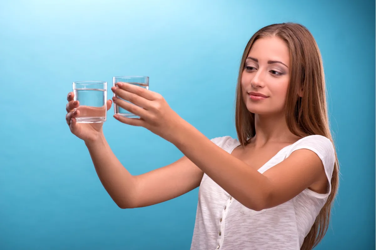Woman holding and comparing two glasses of water against a blue background.